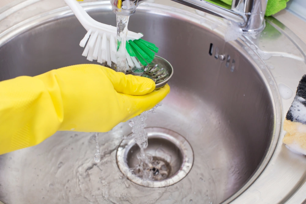 Close up of female hands with protective gloves scrubbing and cleaning kitchen drain
